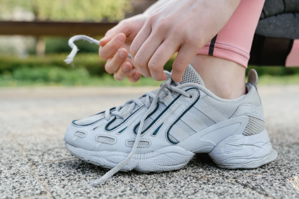 Zbliżenie na kobietę w sportowym stroju, wiążącą białe sneakersy podczas ćwiczeń na zewnątrz.